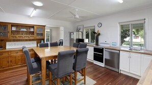 A modern kitchen with a dining area, wooden cabinets, and a view of the outdoors. - Beach Shack From Yesteryear With All The Modern Comforts (Amity Point)