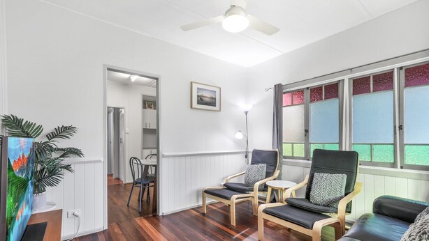 A room with a wooden floor, two chairs with cushions, a black sofa, a ceiling fan, and a window with colored glass. - Perfect for retired folk, Fisherman & Small families (Amity Point)