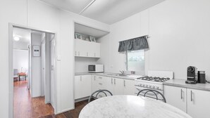 A compact kitchen with white cabinets, a gas stove, a microwave, and a coffee machine. - Perfect for retired folk, Fisherman & Small families (Amity Point)