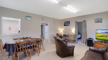 Una sala de estar con comedor, un sofá, un televisor y una escalera que conduce a otra habitación.