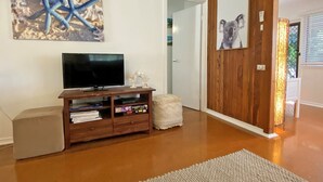 Un salon avec un téléviseur à écran plat posé sur un meuble en bois, un pouf blanc et un tapis.