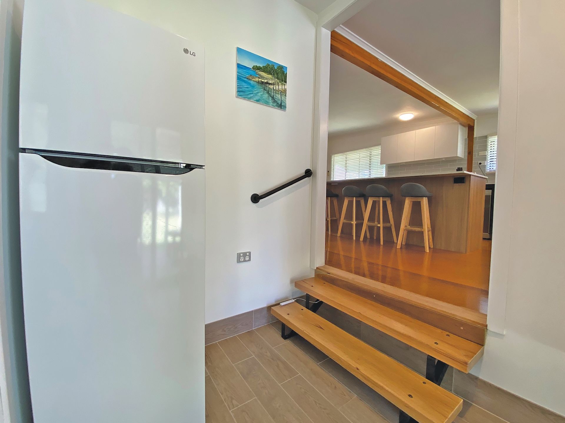 Eine moderne Küche mit einem weißen Kühlschrank, einer hölzernen Bank und einem Bild an der Wand.