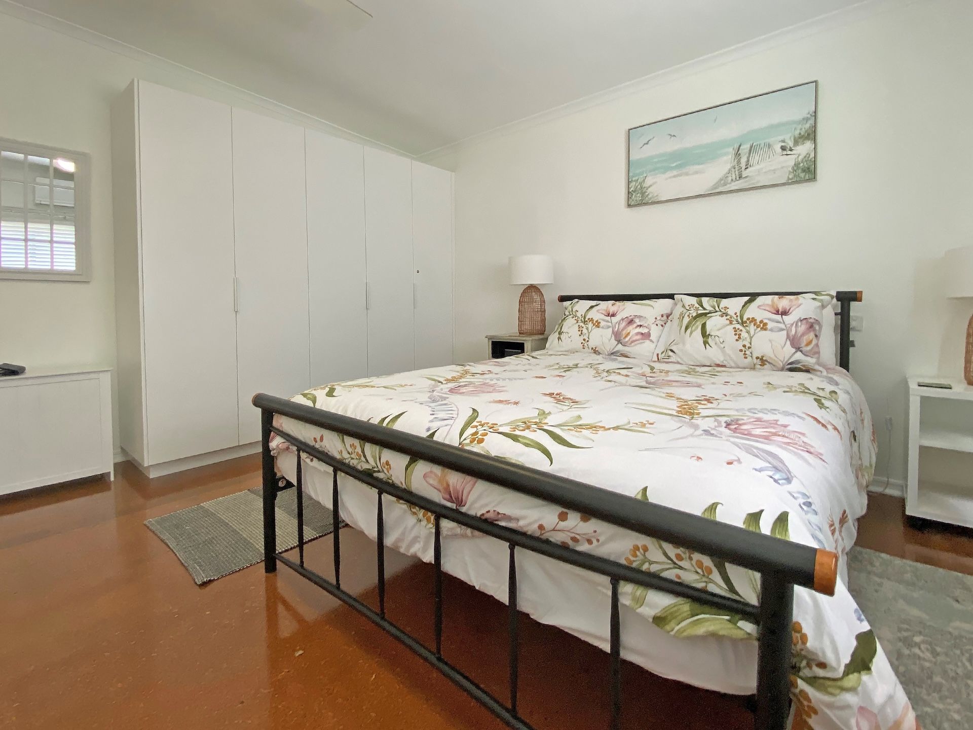 A bedroom with a bed, a wardrobe, a nightstand, a lamp, and a painting on the wall.