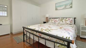 A bedroom with a bed, a wardrobe, a nightstand, a lamp, and a painting on the wall.