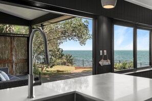 A modern kitchen with a view of the sea, a wooden fence, and a hanging sign. - An Awe-Inspiring Waterfront Retreat (Amity Point)