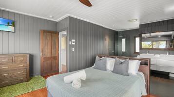Ein Schlafzimmer mit einem Bett, einer Holzkommode, einem Badezimmer mit Spiegel und einem Deckenventilator.