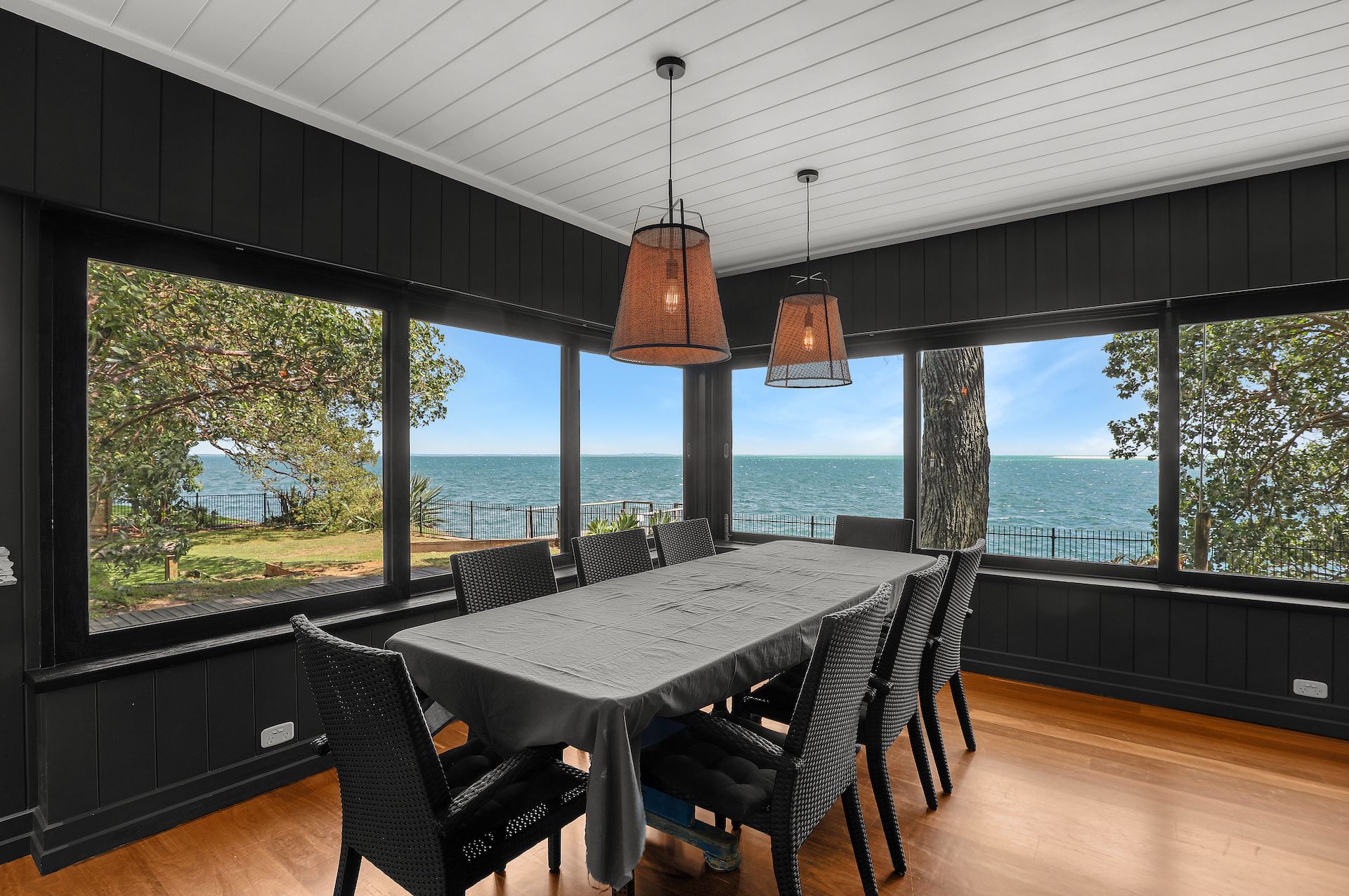 A dining area with a table and chairs, large windows with a view of the sea, and hanging pendant lights.