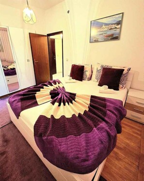 A bedroom with a bed, a wardrobe, a mirror, a painting, and a door.