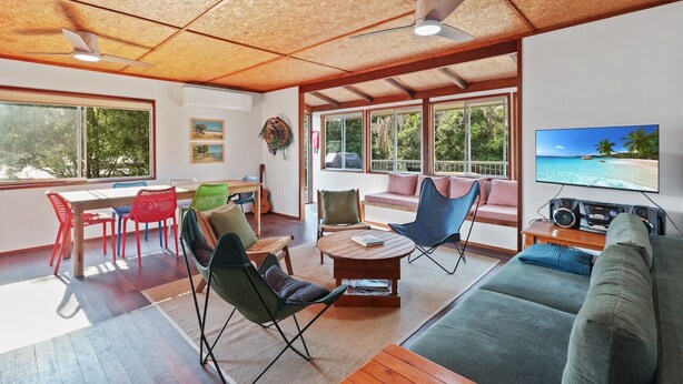 A spacious living area with a wooden ceiling, large windows, a television, and various seating options. - Classic Beach Shack in a Quiet Bush Dune Setting (Amity Point)