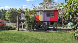 A colorful, elevated house with a staircase leading to a balcony. - Classic Beach Shack in a Quiet Bush Dune Setting (Amity Point)
