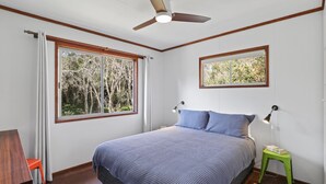 A bedroom with a bed, two windows, a ceiling fan, and a nightstand. - Classic Beach Shack in a Quiet Bush Dune Setting (Amity Point)
