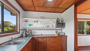A compact kitchen with wooden cabinets, a built-in microwave, and a coffee machine. - Classic Beach Shack in a Quiet Bush Dune Setting (Amity Point)