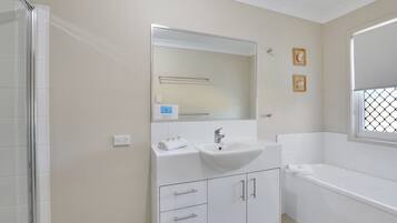 Un baño con lavamanos, espejo, toallero y bañera.