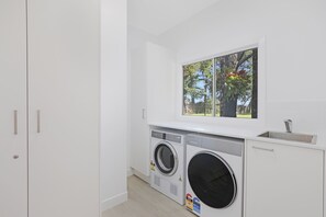 A laundry room with two washing machines, a window with a view of trees, and a sink. - Amity Waterfront on 1/2 Acre (Amity Point)