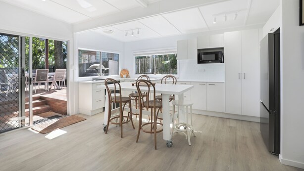 Une cuisine moderne avec des meubles blancs, un réfrigérateur noir et un coin repas comprenant une table et des chaises.