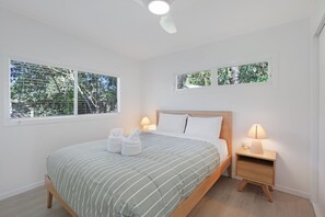 Une chambre à coucher avec un lit, deux tables de chevet avec des lampes et deux fenêtres équipées de stores.