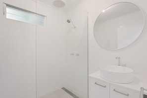 Un bagno moderno con cabina doccia in vetro, uno specchio rotondo e un lavandino bianco.