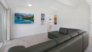 Un salon moderne avec un canapé d’angle, un téléviseur à écran plat et trois tableaux représentant des paysages accrochés au mur.