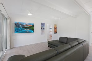 Un salon moderne avec un canapé d’angle, un téléviseur à écran plat et trois tableaux représentant des paysages accrochés au mur.