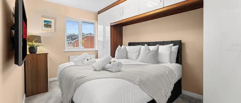 A bedroom with a bed, a television, a window, and a wardrobe.