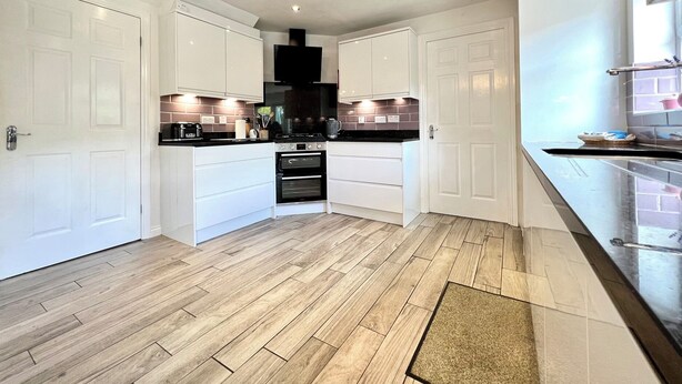 A modern kitchen with white cabinetry, a black stove, and a wooden floor. - Harefield (Morpeth)
