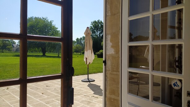 A view through a window with a view of a grassy area, a patio, and a building with multiple windows.