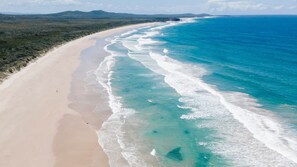 An aerial view of a beach with clear turquoise waters and a sandy shore.