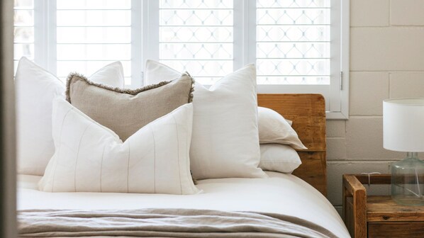 A neatly made bed with white linens and a wooden headboard, positioned next to a window with a geometric pattern.
