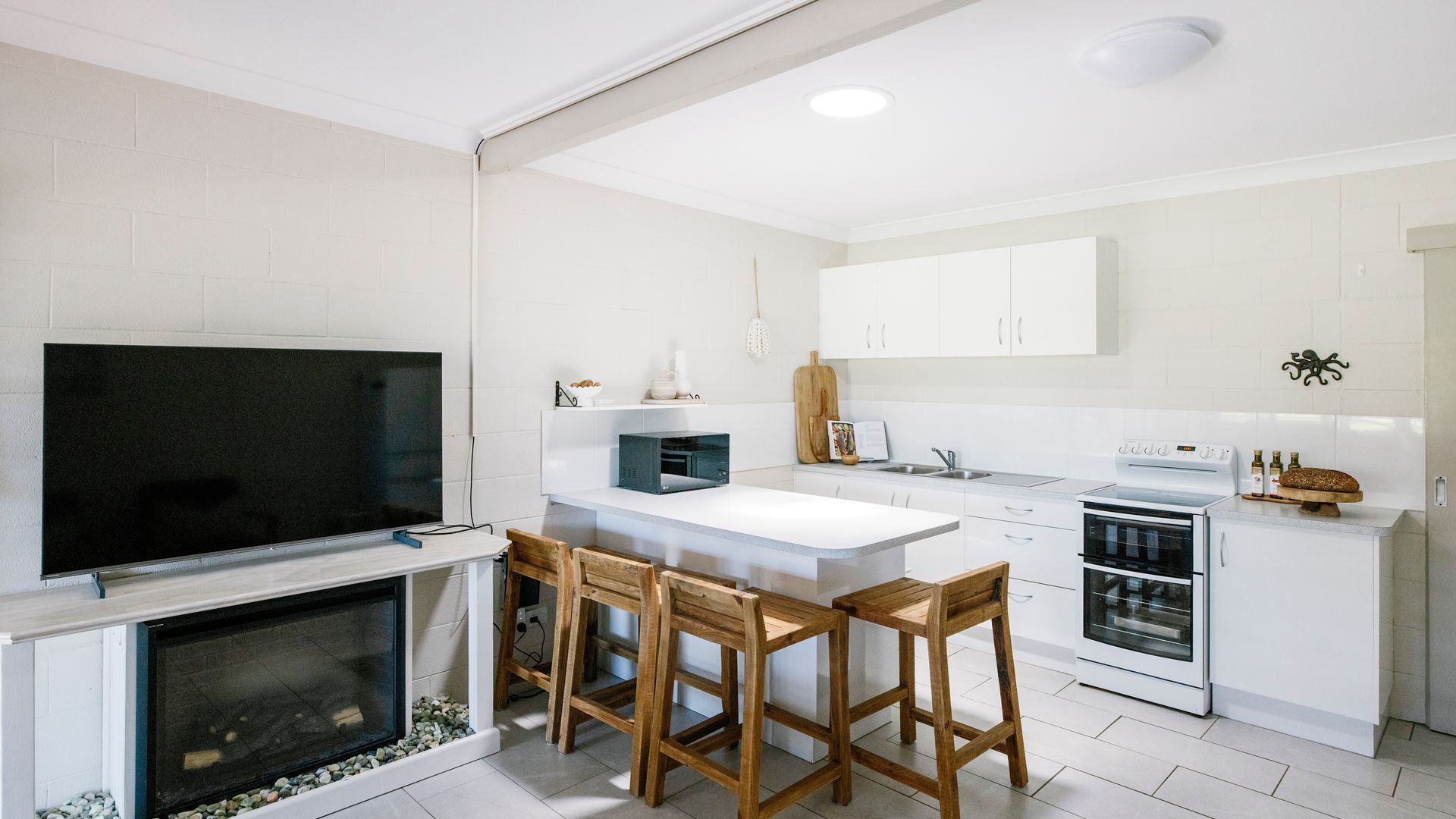 A modern kitchen with white cabinetry, a large TV, a microwave, and a dining area with wooden chairs.