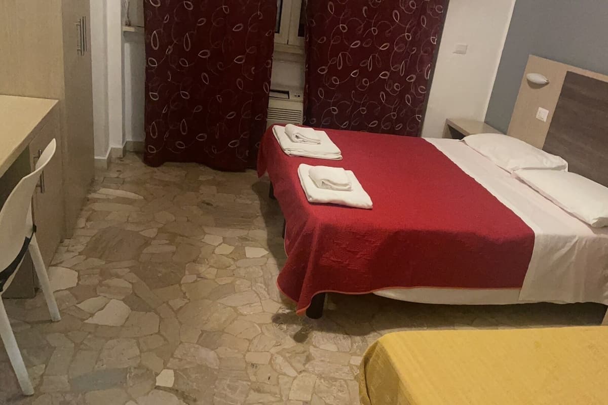 A small hotel room with a bed, a desk, and a chair. There are towels on the bed.