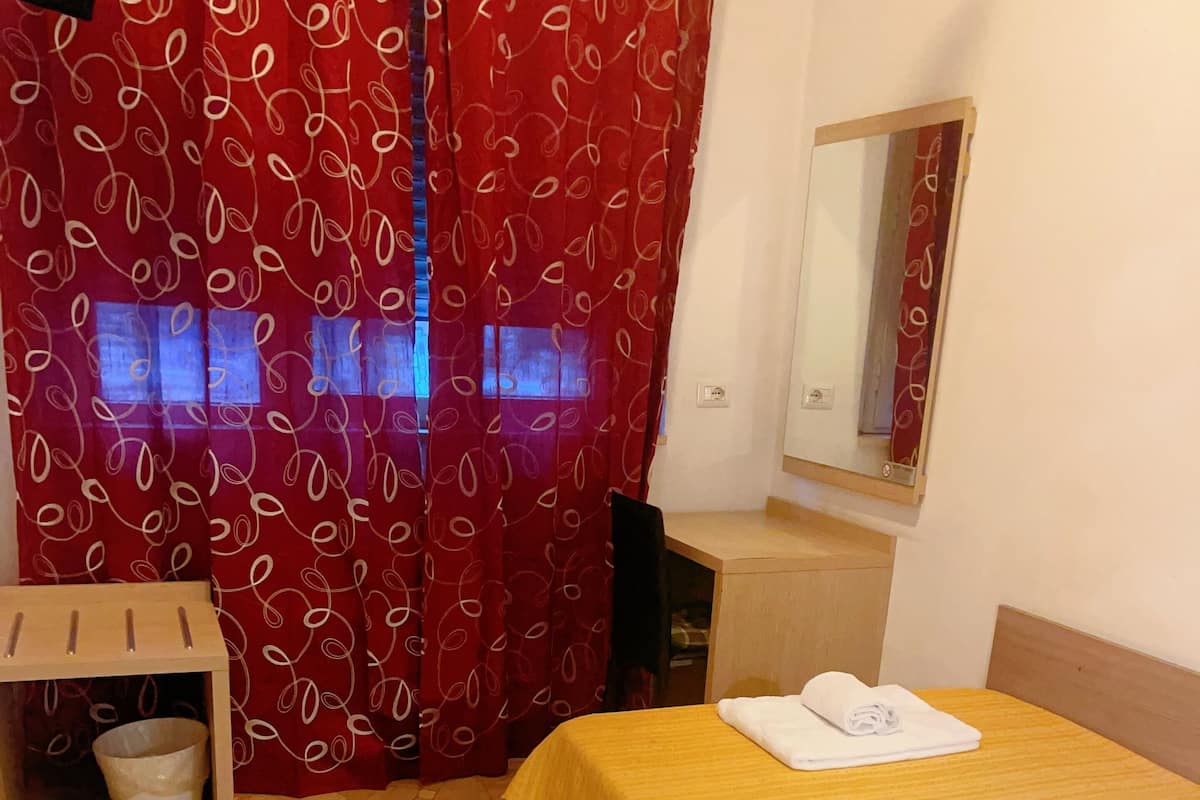 A hotel room with a bed, a desk, a chair, a small table, and a tiled floor.