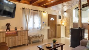 A cozy living room with a wooden ceiling, a flat-screen TV, a sofa, a coffee table, and a stone wall. - Mareu Stonehouse in the Cretan countryside (Stironas)