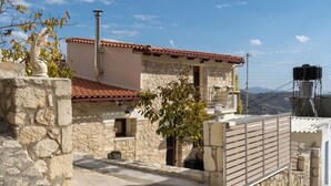 A stone building with a red-tiled roof, a small balcony, and a water tank on the roof. - Mareu Stonehouse in the Cretan countryside (Stironas)