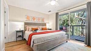A bedroom with a bed, a nightstand, a ceiling fan, a window with a view of trees, and a sliding glass door leading to an outdoor area. - The Salty Mint - Resort Condo w/ Pools, Hot Tub, & Beach Access – Sleeps 7 (Kure Beach)