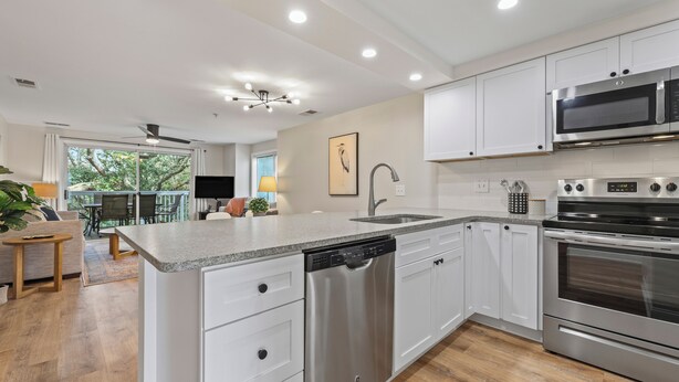 A modern kitchen with white cabinets, stainless steel appliances, and a central island with a dishwasher. - The Salty Mint - Resort Condo w/ Pools, Hot Tub, & Beach Access – Sleeps 7 (Kure Beach)