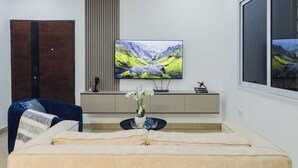 Moderni olohuone, jossa on sohva, sininen nojatuoli, seinälle asennettu televisio ja koristeellinen maljakko sivupöydällä.