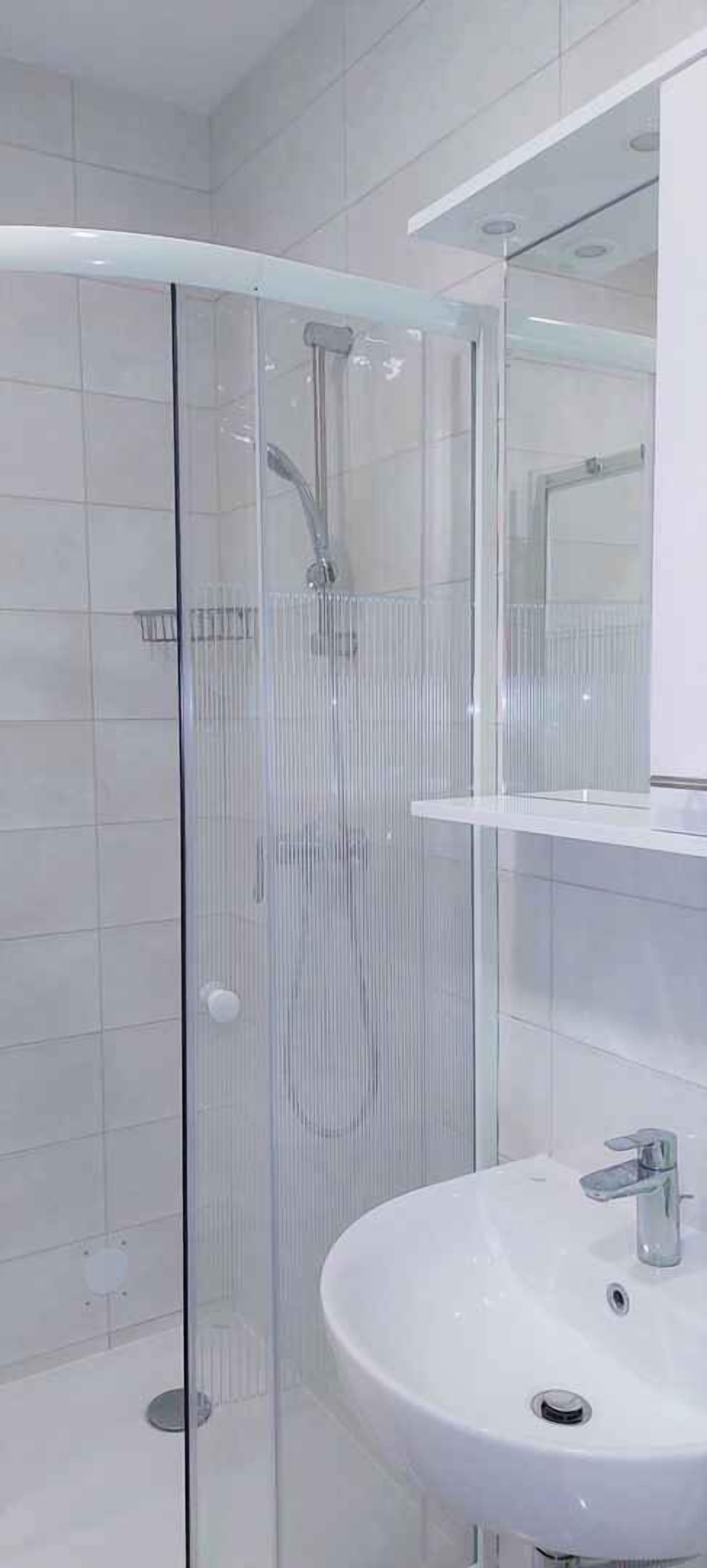 A modern bathroom with a glass-enclosed shower, a white sink, and a mirror above the sink.
