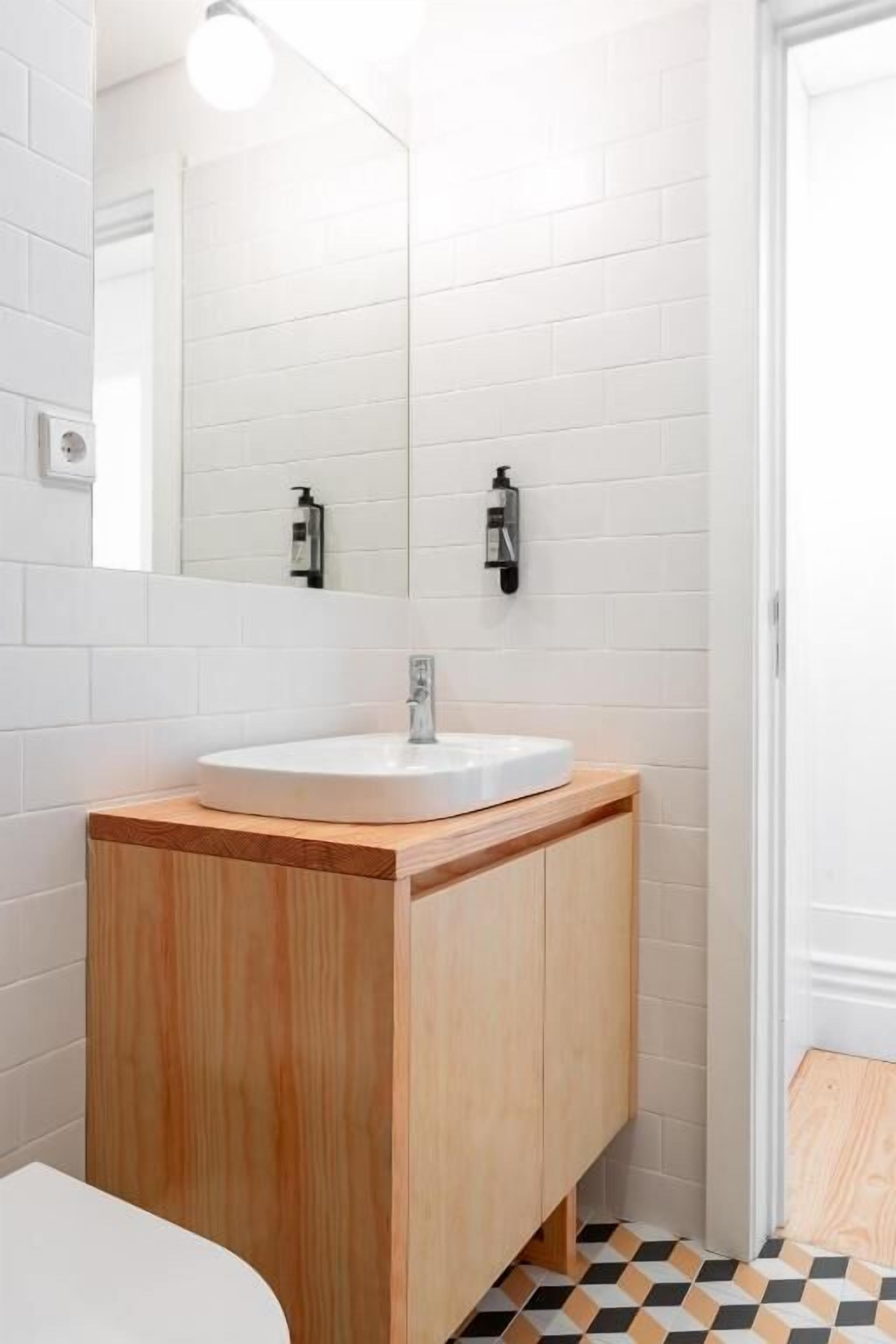 Een badkamer met een witte wastafel, een houten wastafelmeubel en een spiegel.