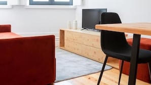 A modern living room with a wooden floor, a red sofa, a black chair, a wooden table, and a TV on a wooden cabinet.
