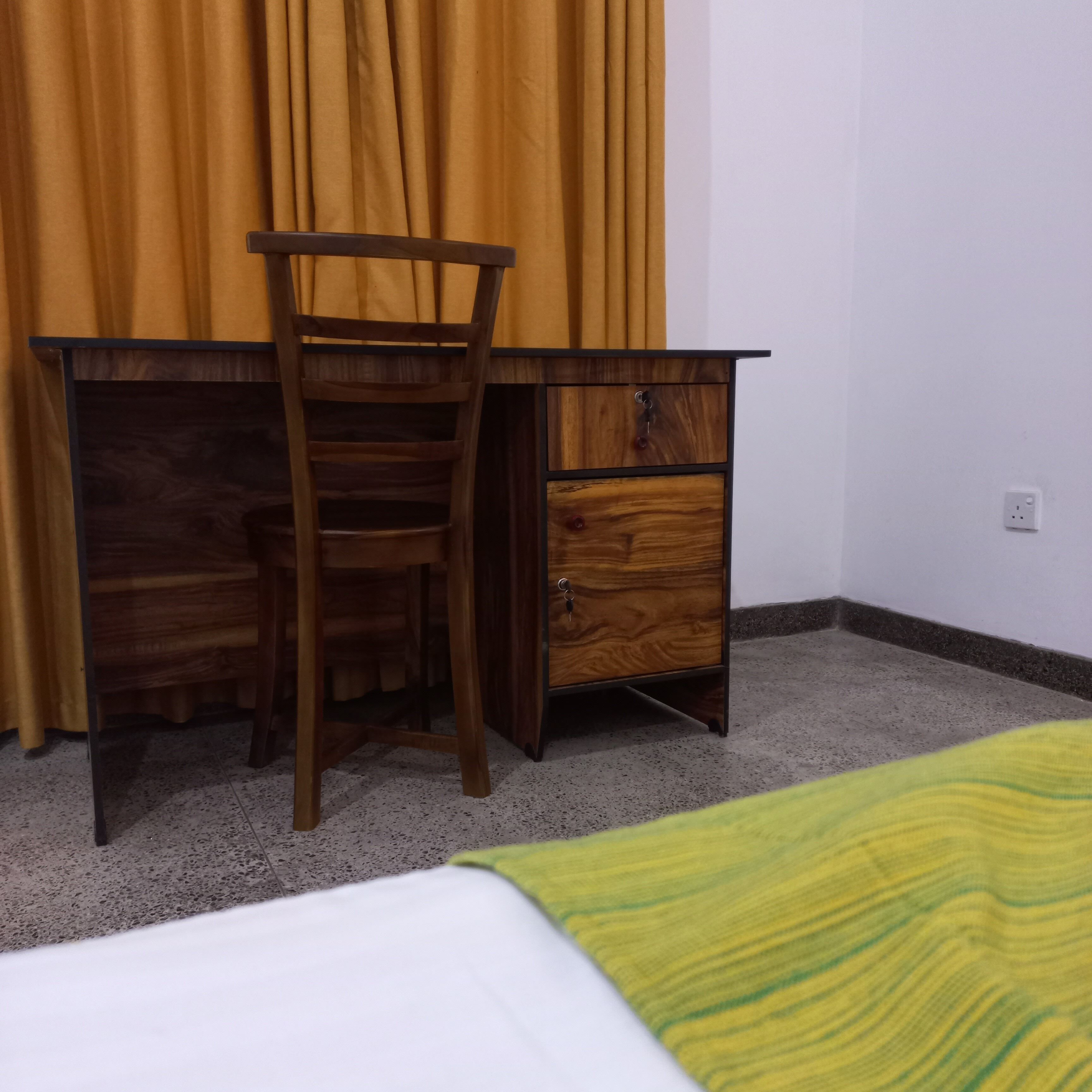 Un escritorio de madera con una silla, un cajón y una cama con una colcha verde.