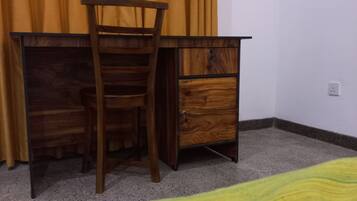 Un escritorio de madera con una silla, un cajón y una cama con una colcha verde.