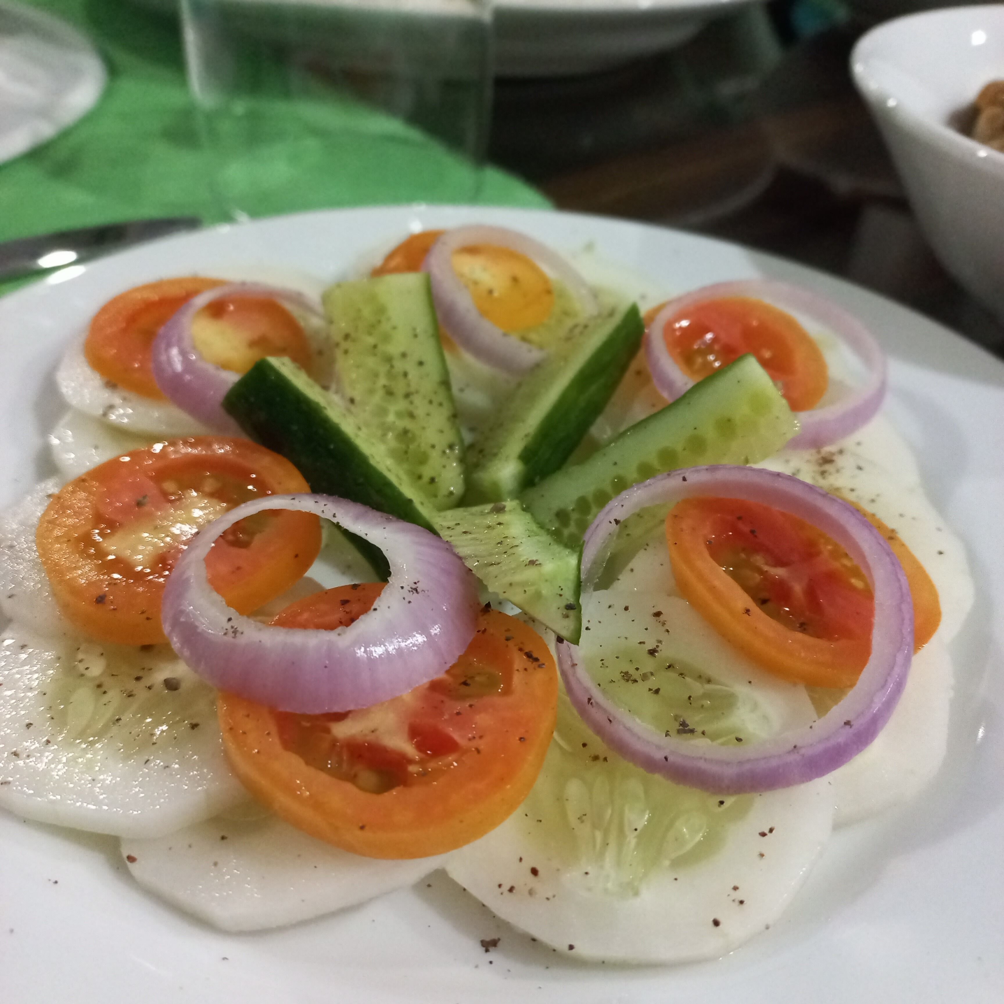 A plate of food with sliced cucumbers, tomatoes, and onions arranged on a white plate.