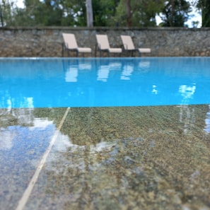 Una piscina cristalina con un muro de piedra y sillones de descanso al fondo.