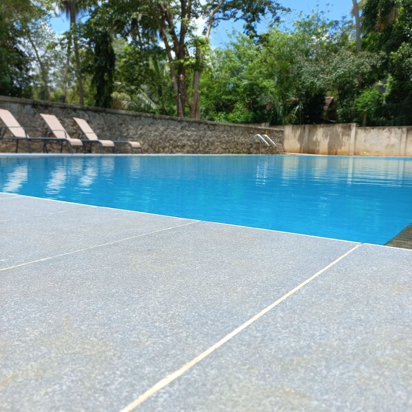 Una piscina con un muro de piedra y sillones de descanso al fondo.
