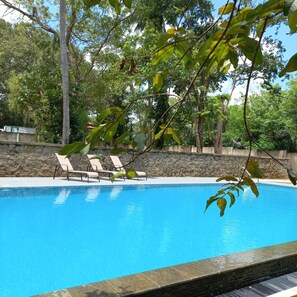 Una piscina con sillas de descanso y un muro de piedra al fondo.