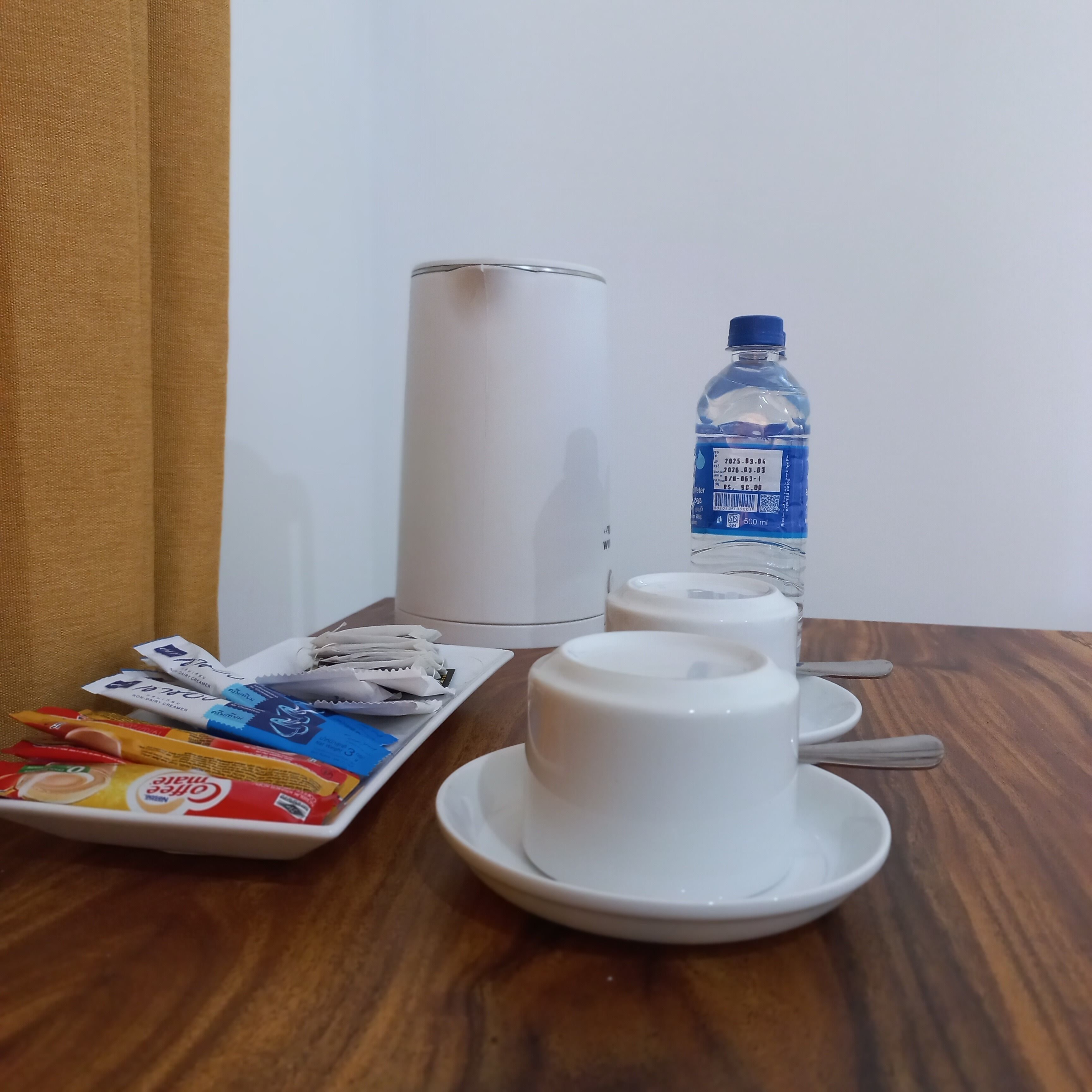 A table with a water bottle, a plate of snacks, and a white cup.