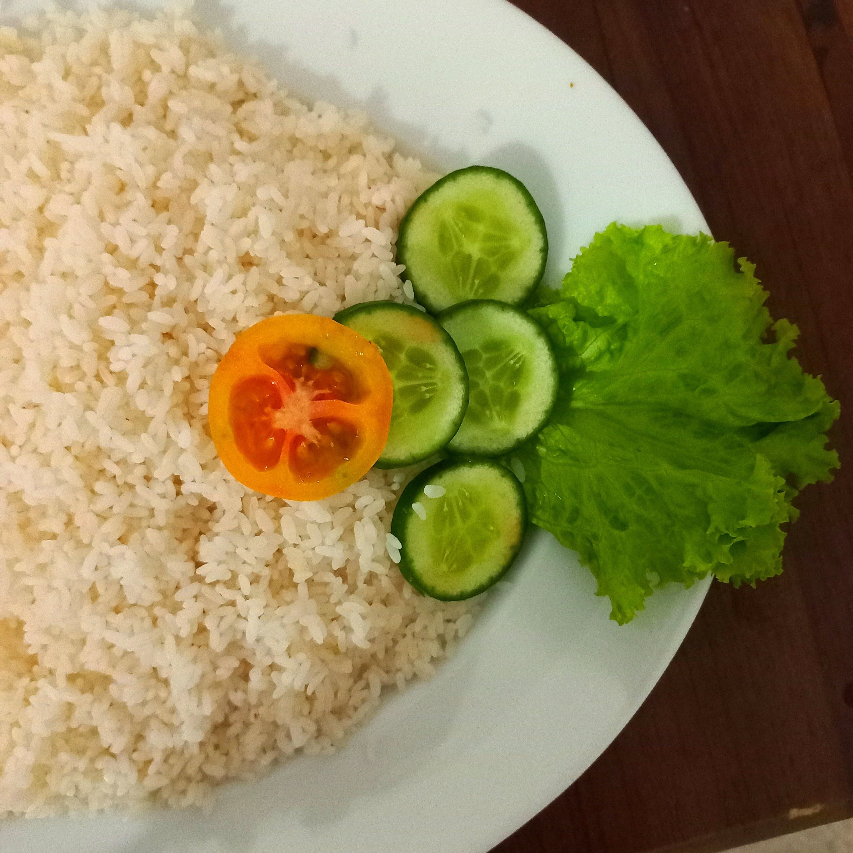 Un plato de arroz blanco con una rodaja de tomate y pepino, y una hoja de lechuga.