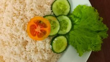 Un plato de arroz blanco con una rodaja de tomate y pepino, y una hoja de lechuga.