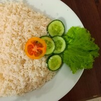 Un plato de arroz blanco con una rodaja de tomate y pepino, y una hoja de lechuga.