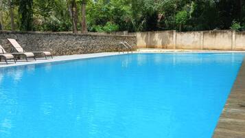 Una piscina azul cristalina con sillas de descanso y un muro de piedra.